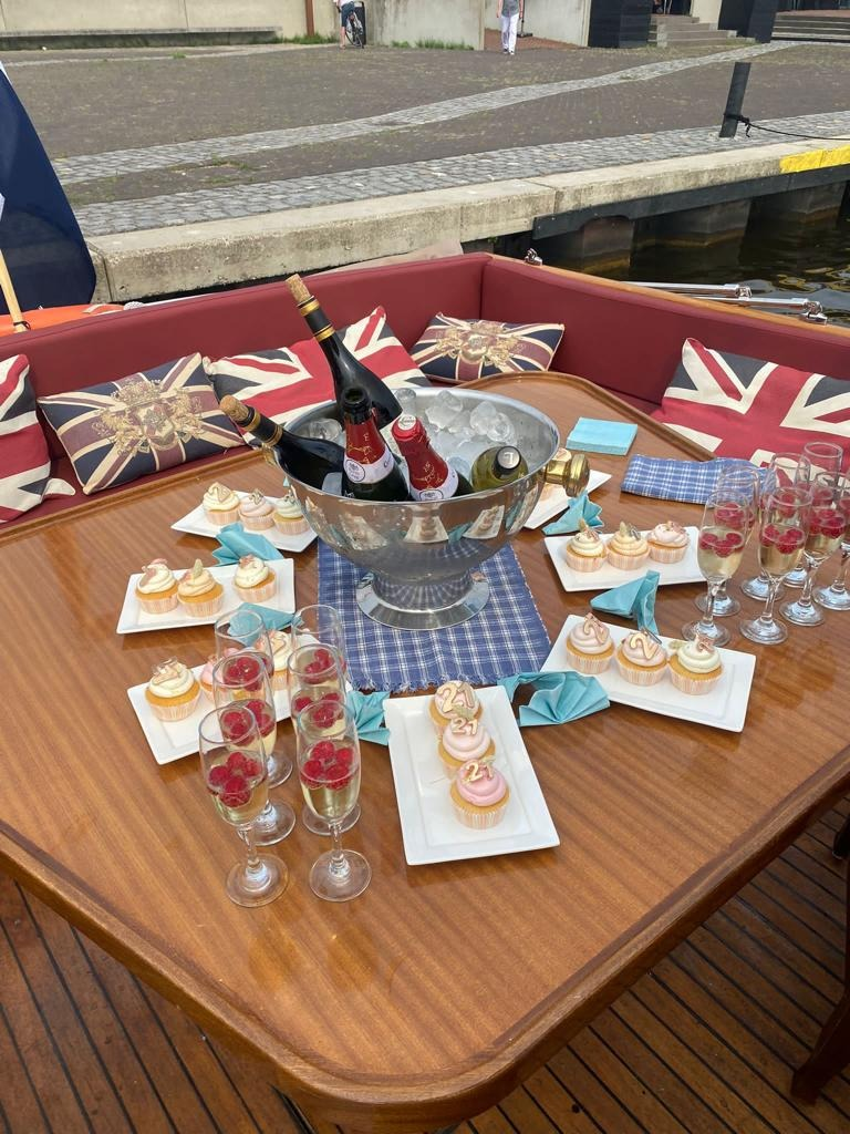 Een houten bootvormige tafel, gedekt voor een feestje, met champagne, cupcakes en glazen op kussens met een Union Jack-thema.