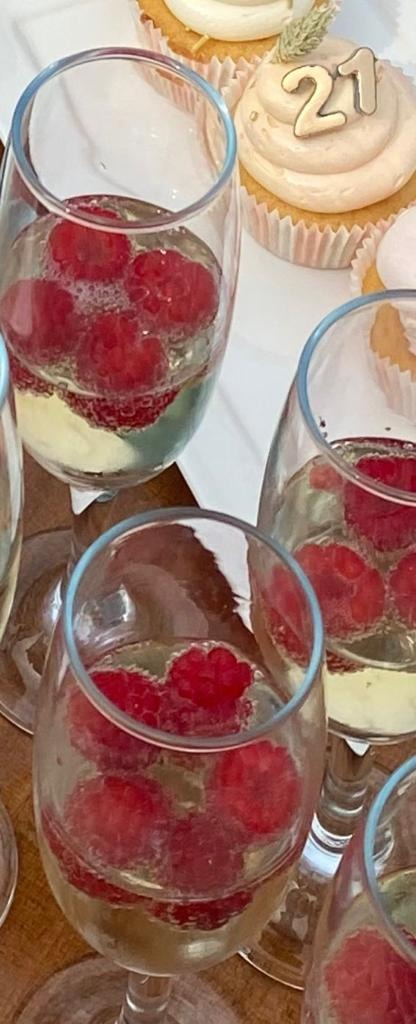 Champagneglazen gevuld met mousserende wijn en verse frambozen, naast cupcakes met een 