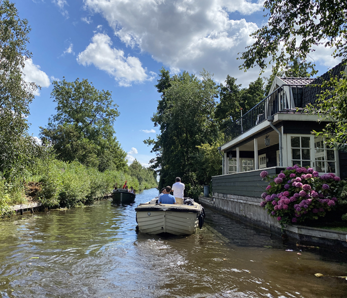 Twee kleine bootjes varen door een smal kanaal, omzoomd door weelderig groen en een charmant huis met roze hortensia's.