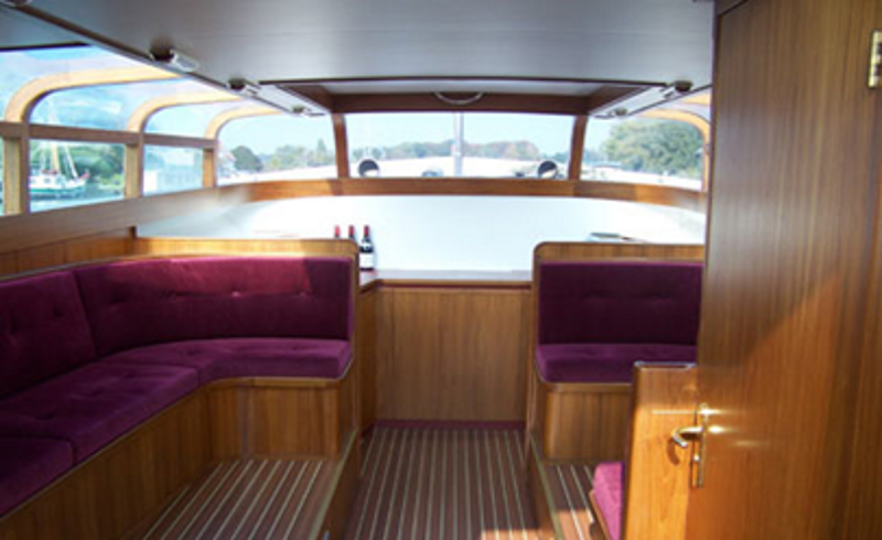 Interieur van een bootkajuit met houten wanden, gestreepte vloer en paarse fluwelen U-vormige zitbanken bij panoramische ramen.