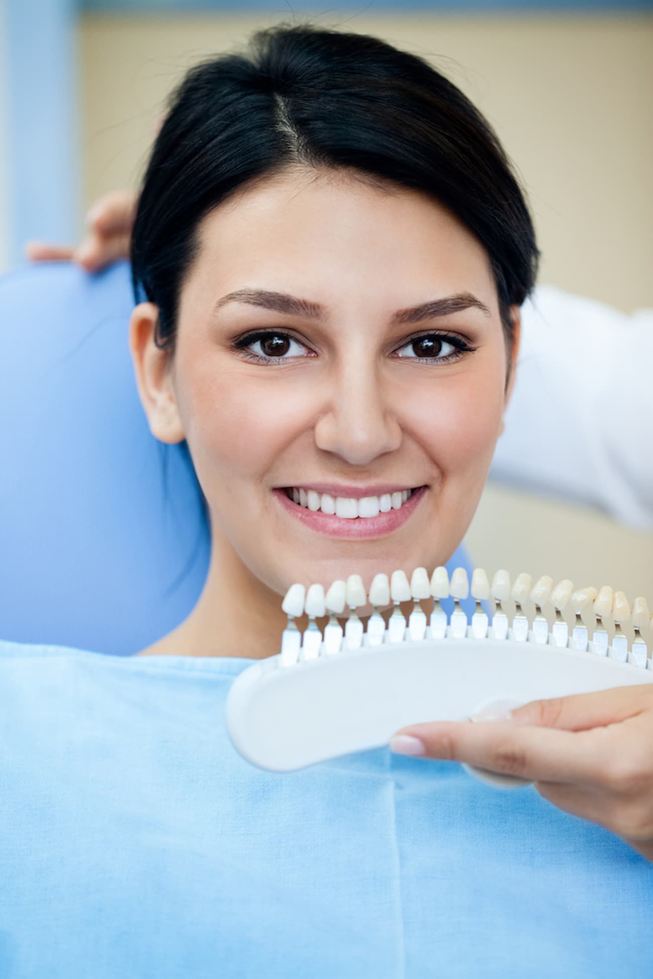 A Woman Is Sitting in A Dental Chair Holding a Tooth Color Chart — Cane to Coast Dentures in Sarina, QLD