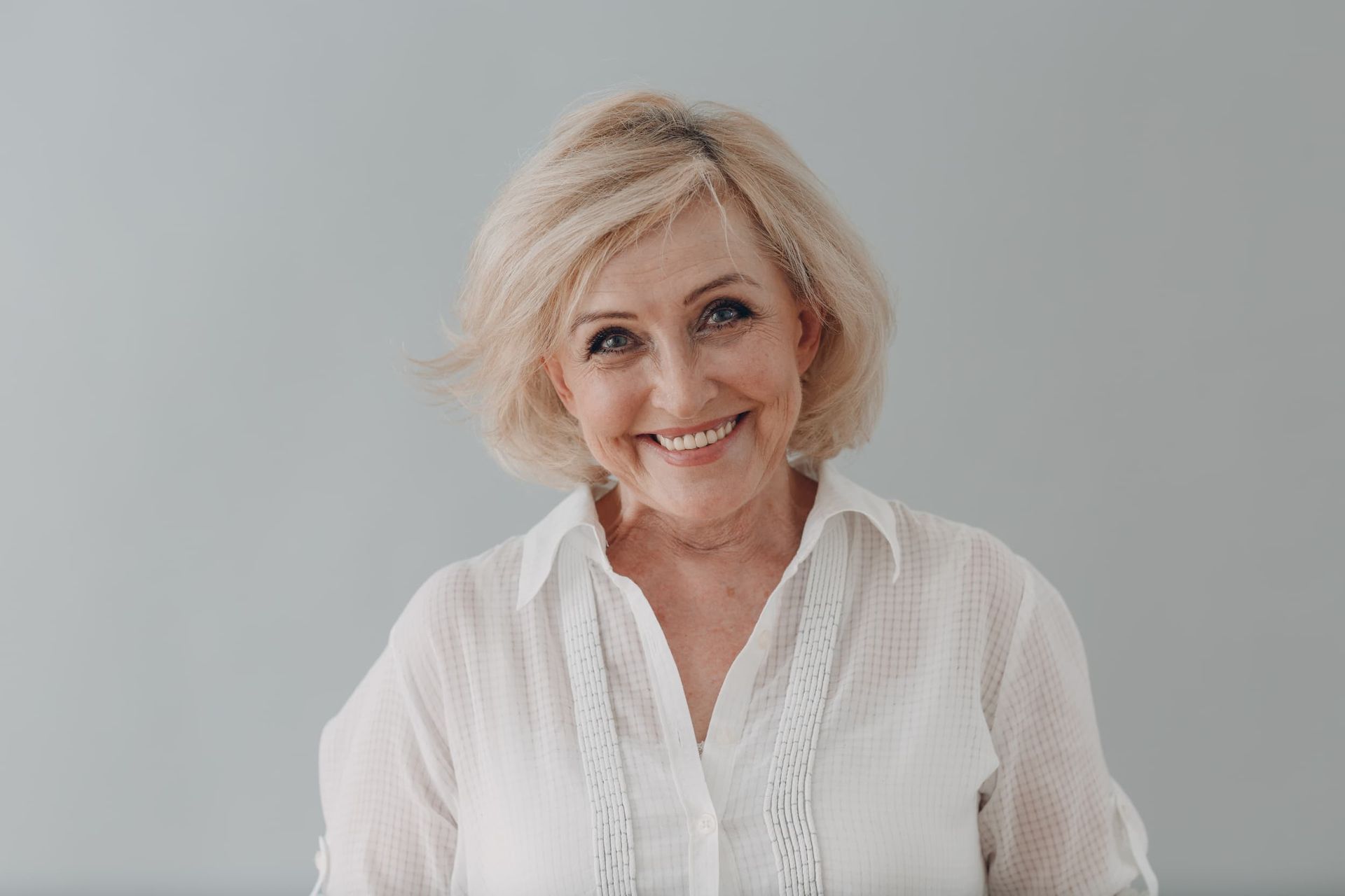 An Elderly Woman in A White Shirt Is Smiling and Looking at The Camera — Cane to Coast Dentures in Moranbah, QLD