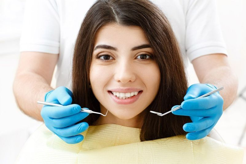 A Woman Is Sitting in A Dental Chair While a Dentist Examines Her Teeth — Cane to Coast Dentures in Sarina, QLD