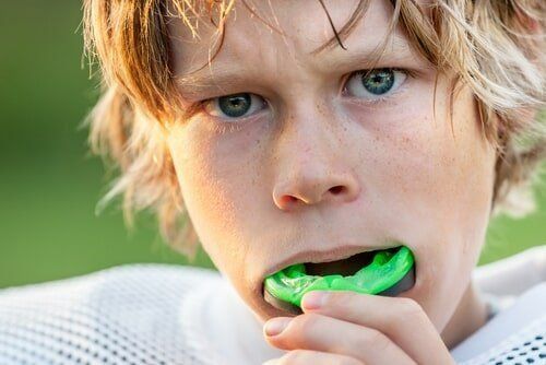 A Young Boy Is Wearing a Green Mouth Guard — Cane to Coast Dentures in Sarina, QLD