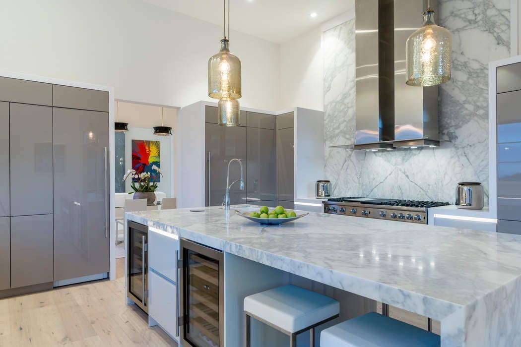 Modern kitchen featuring a marble-topped island, grey cabinetry, stainless steel appliances, and two hanging glass pendants.