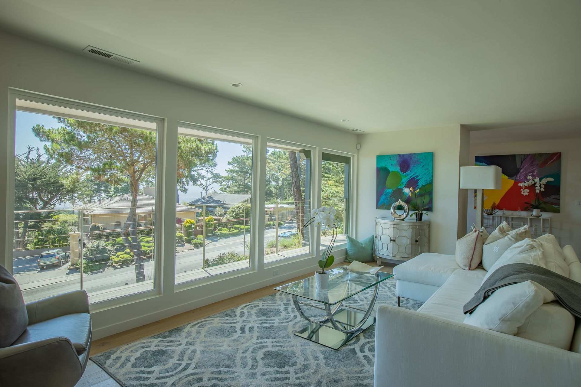 Bright living room with large windows, white sofas, colorful art, and an ocean view