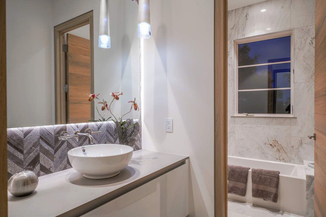 A modern bathroom with a white vessel sink on a vanity, marble wall tiles, a bathtub, and warm-toned wood door frames.