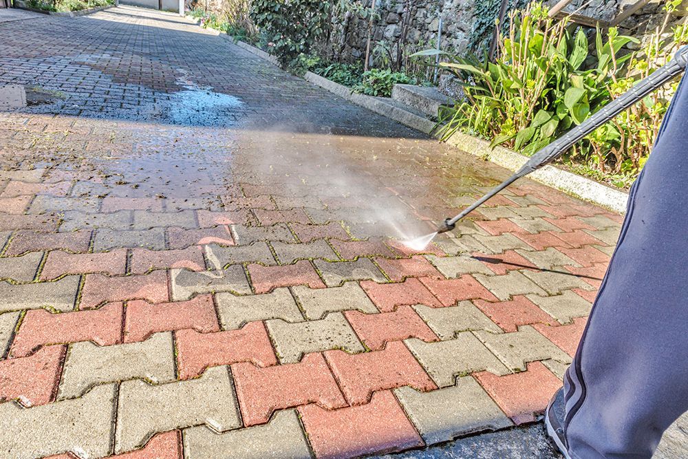 A person is using a high pressure washer to clean a brick walkway.