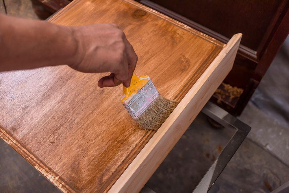A person is painting a wooden drawer with a brush.