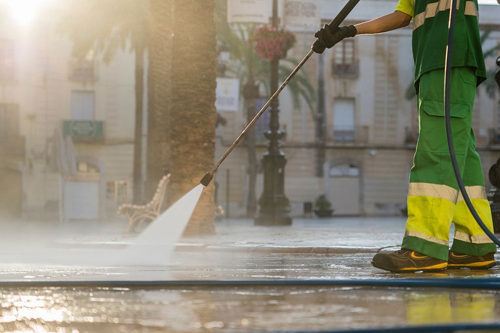 A man is using a high pressure washer to clean a sidewalk.