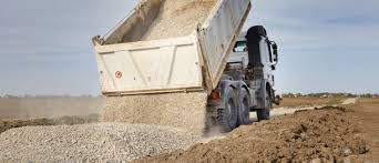 A dump truck is dumping dirt on a dirt road.