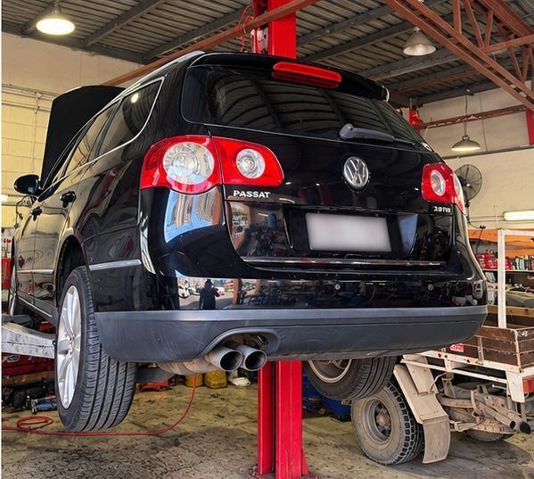 Black Volkswagen hatchback lifted on a shop hoist in a garage, rear view with dual exhaust. — Mechanic In Noosaville, QLD