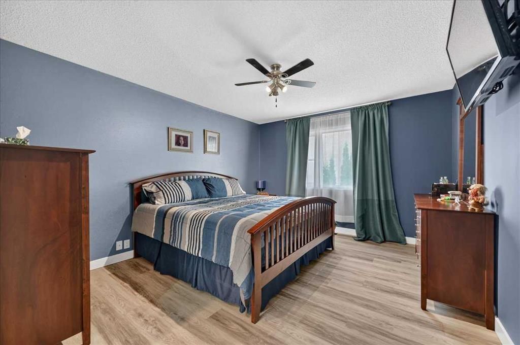 Bedroom with blue walls, wood bed frame, ceiling fan, dresser, and sliding glass door with curtains.