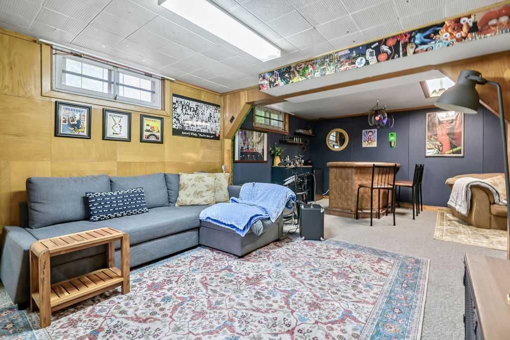 Cozy basement family room with gray sectional, patterned rug, blue chair, and dining area beyond