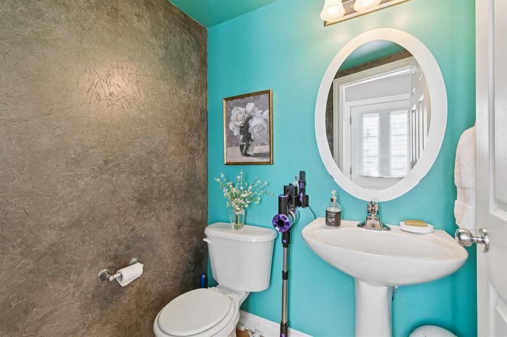 Small bathroom with turquoise walls, pedestal sink, toilet, round mirror, and textured shower wall