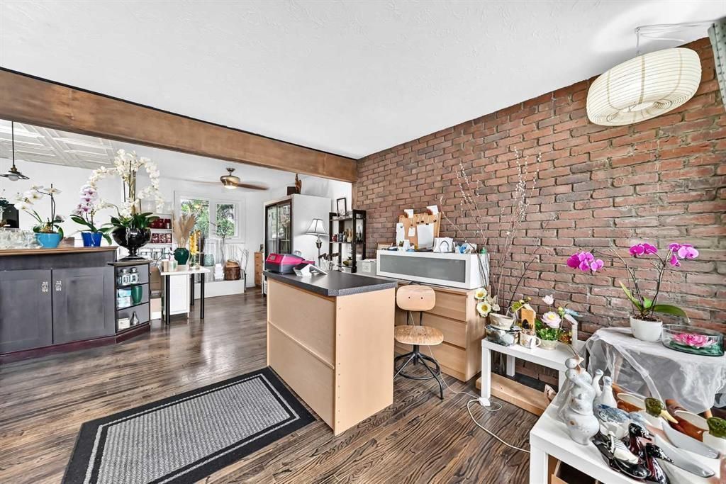 Bright living room with exposed brick wall, desk, plants, and patterned rug in a modern home interior