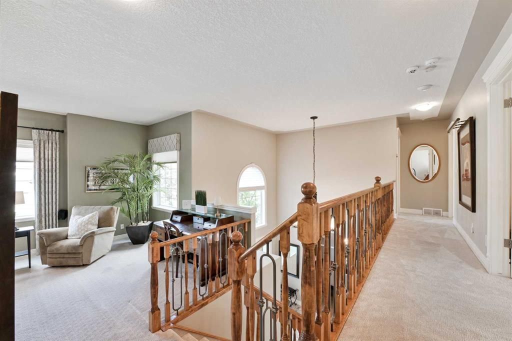 Bright upstairs landing overlooking living room, with wooden railing, beige walls, and carpeted hallway.