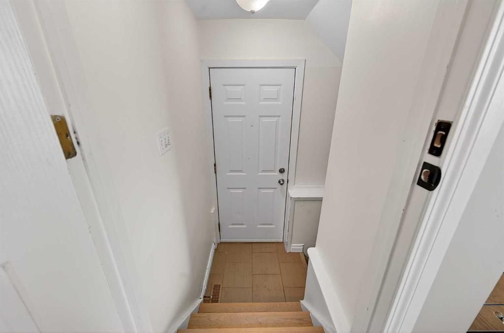 Narrow white hallway with stairs leading down to a closed white door at the bottom.