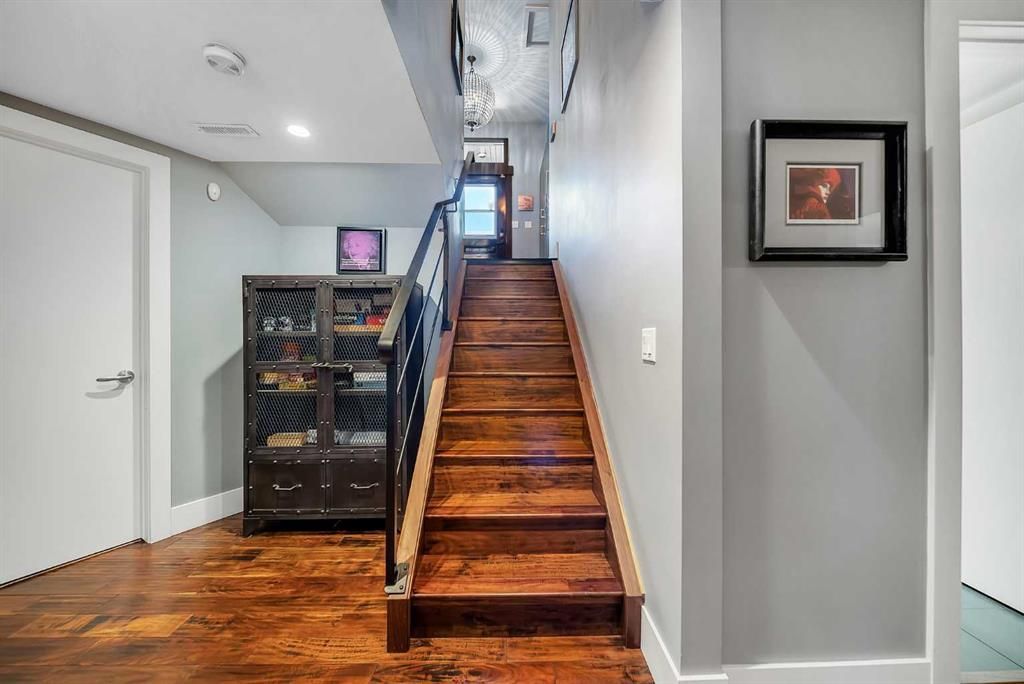 Interior hallway with wooden stairs, black railing, gray walls, and framed artwork.
