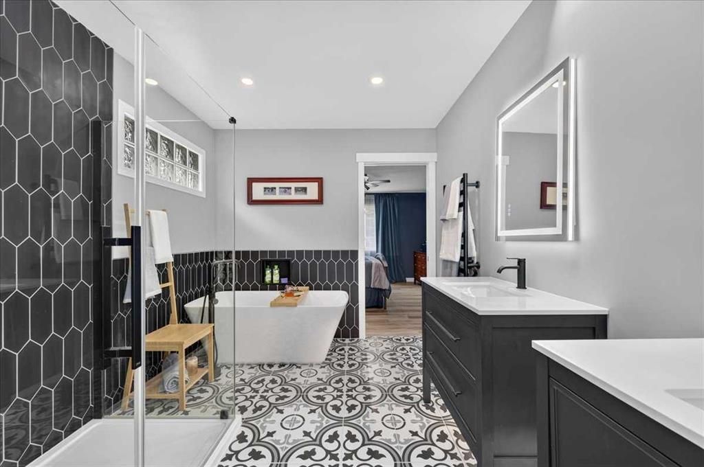 Modern bathroom with black-and-white tile, vanity, large mirror, and freestanding tub by a striped bench.