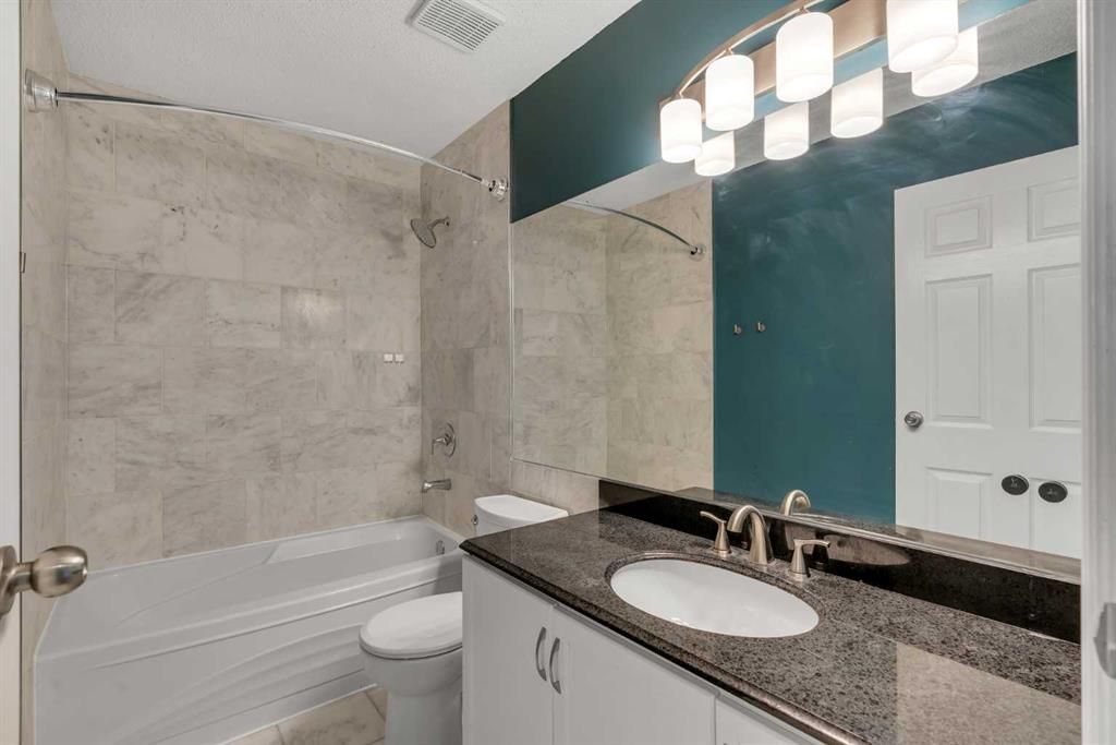 Small bathroom with bathtub, granite vanity, teal accent wall, and white double vanity lights