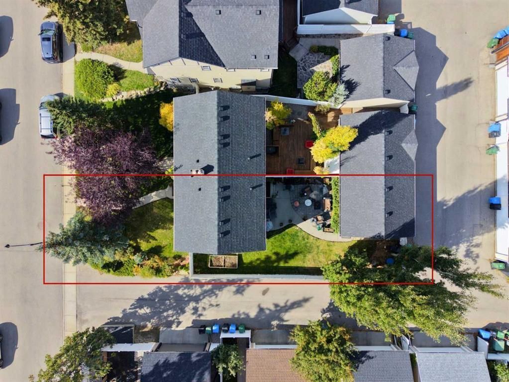 Aerial view of a suburban house with a driveway, trees, and parked cars on the street.