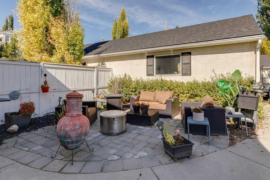 Backyard patio with outdoor seating, fire pit, potted plants, and a barbecue grill under a sunny sky