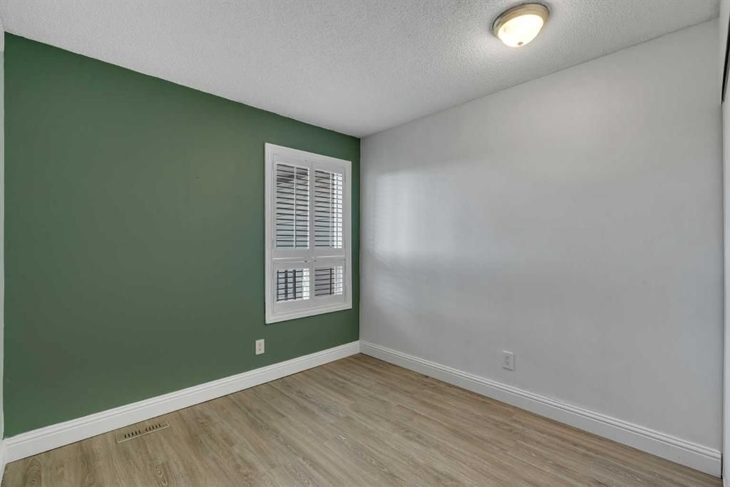 Empty room with green accent wall, white walls, wood floor, and a window with shutters