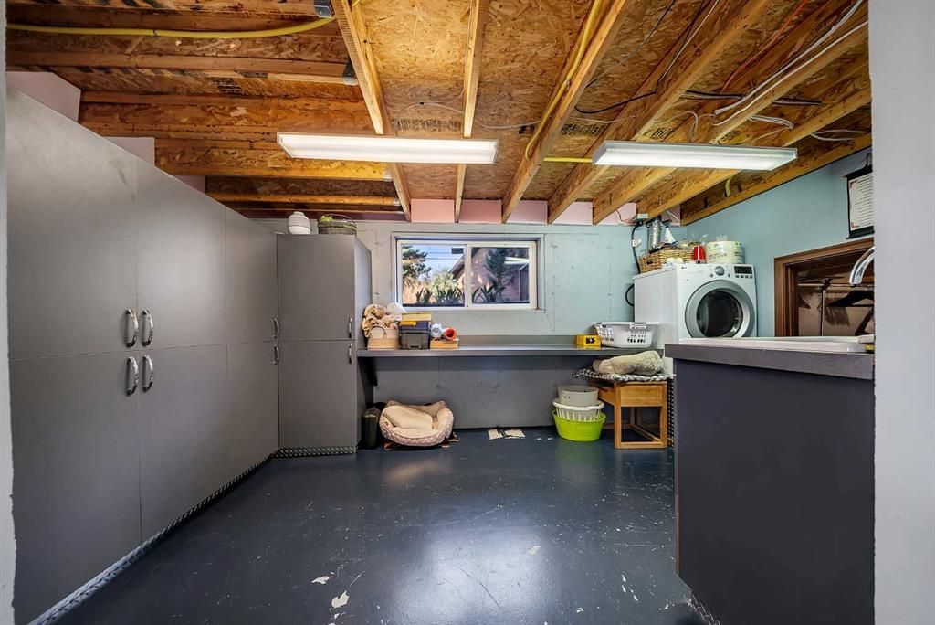 Basement laundry room with washer, sink, cabinets, and workbench under exposed ceiling joists