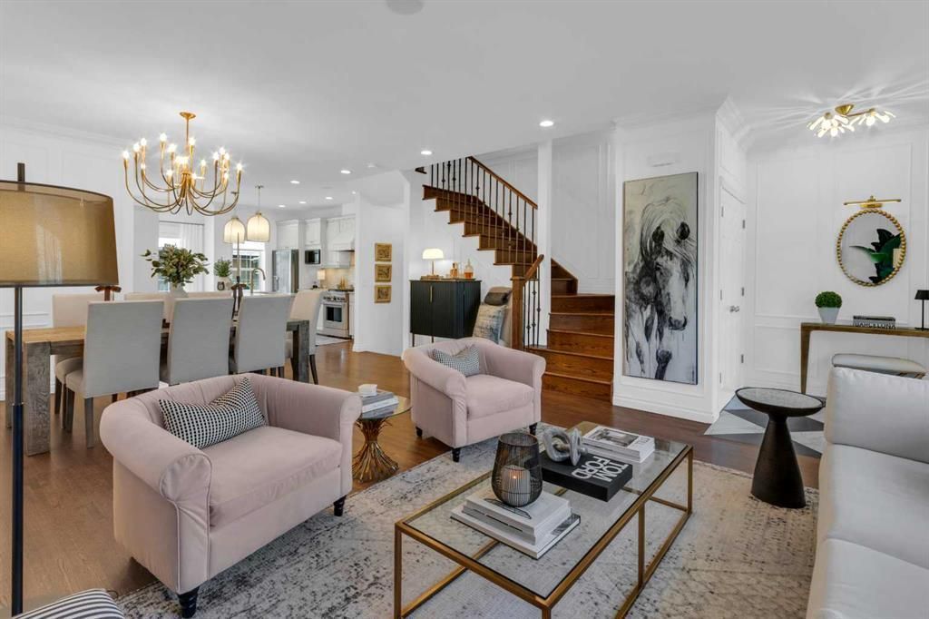 Bright open living room with pink chairs, glass coffee table, staircase, chandelier, and dining area