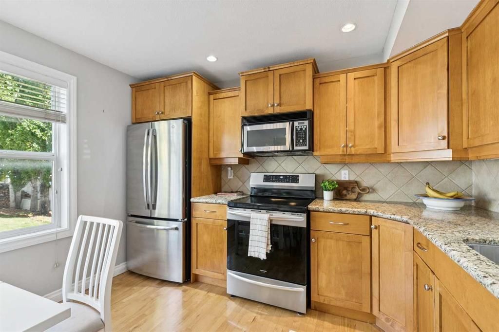 Bright kitchen with wooden cabinets, stainless steel appliances, granite counters, and a dining chair by the window
