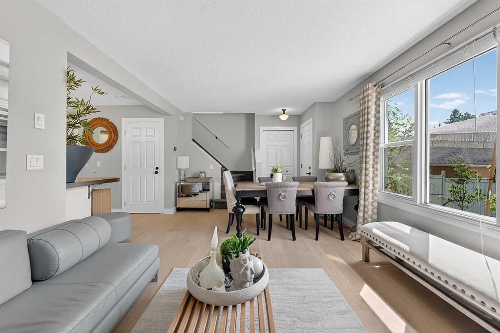 Bright living-dining room with gray sofa, dining table, large windows, and a view of the outdoors