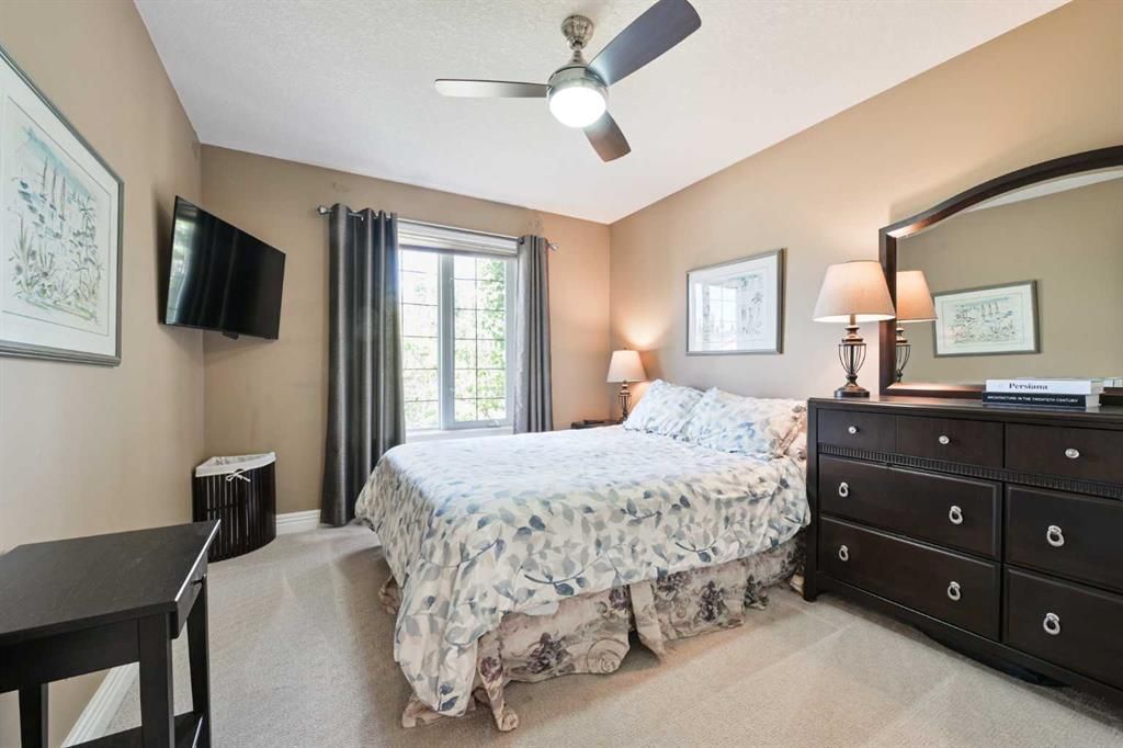 Bedroom with a bed, dresser, wall-mounted TV, ceiling fan, and a window with curtains