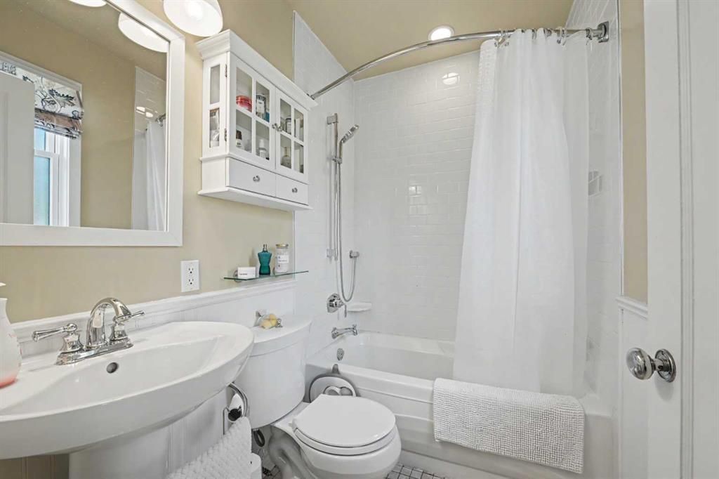 Small white bathroom with sink, toilet, shower curtain, wall mirror, and cabinet.