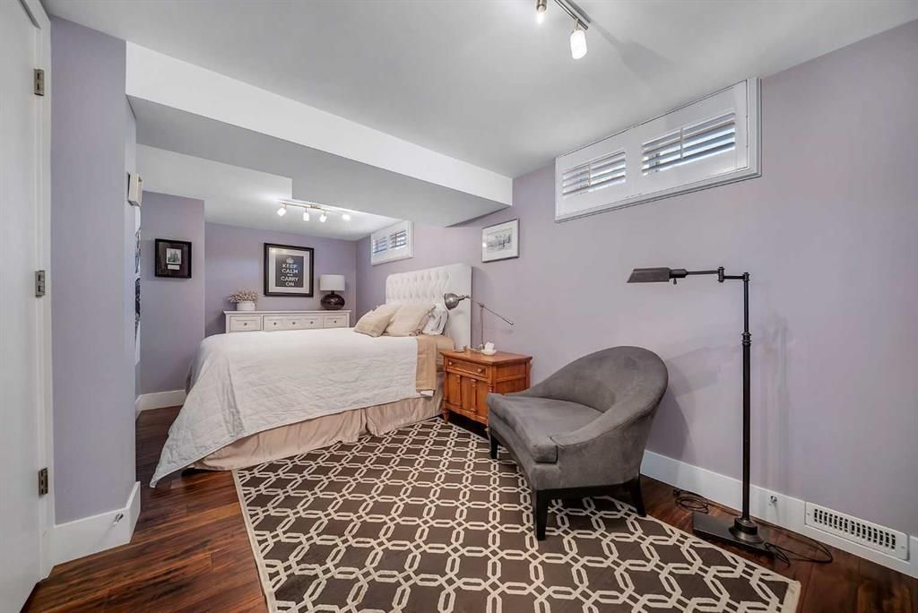 Bedroom with bed, gray chair, floor lamp, and patterned rug in soft purple-gray tones