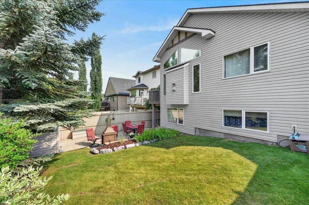 Backyard patio with red chairs beside a beige house and green lawn under a sunny sky