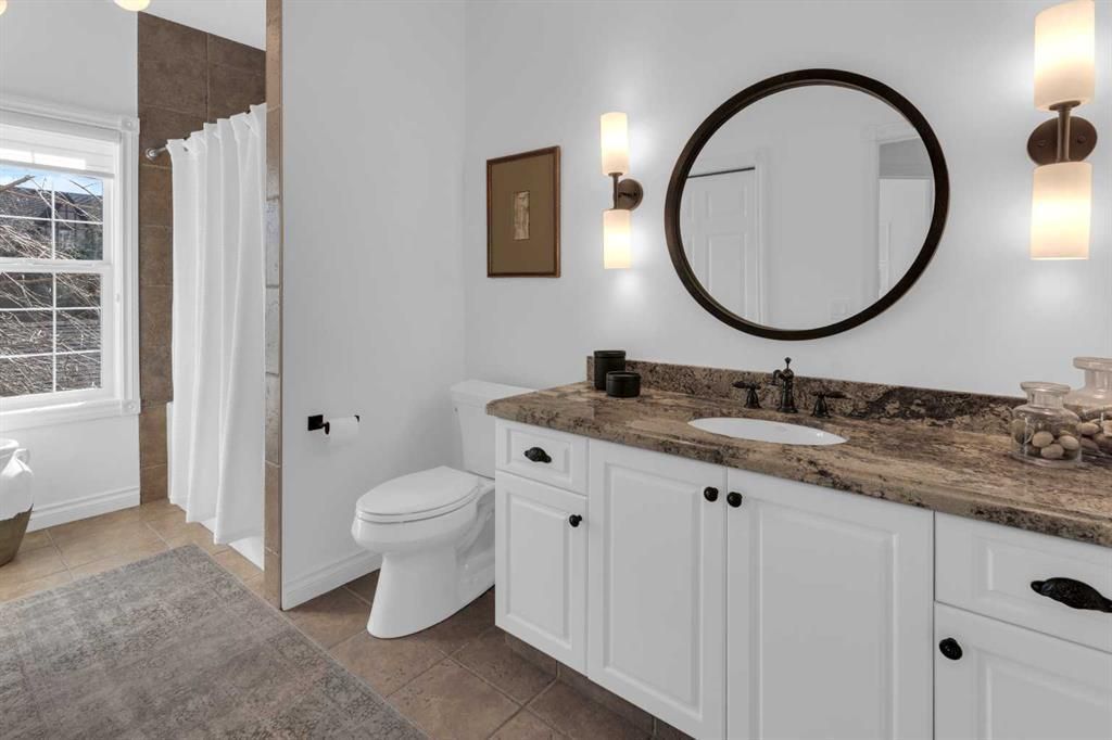 Modern white bathroom with double vanity, round mirror, sconces, and separate toilet area