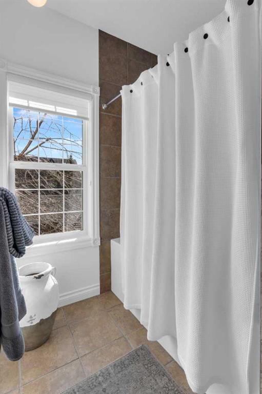 Small bathroom with white shower curtain, beige tile floor, and window beside a toilet