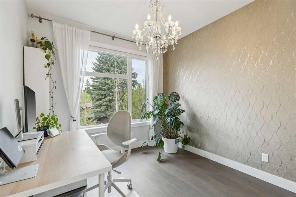 Bright home office with white desk, chair, chandelier, plants, and large window overlooking greenery