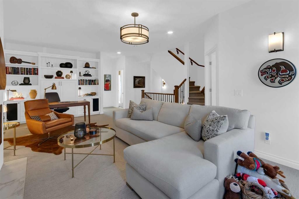 Bright living room with gray sectional, orange chair, fireplace, shelves, and staircase.
