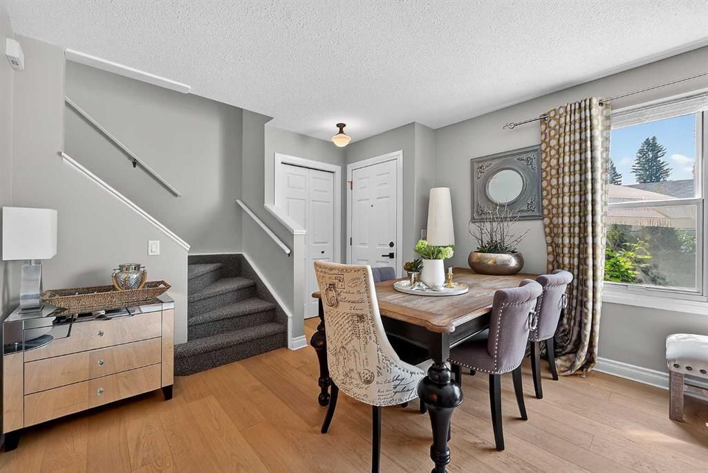 Bright dining room with a table, upholstered chairs, staircase, and large window with a view outside.