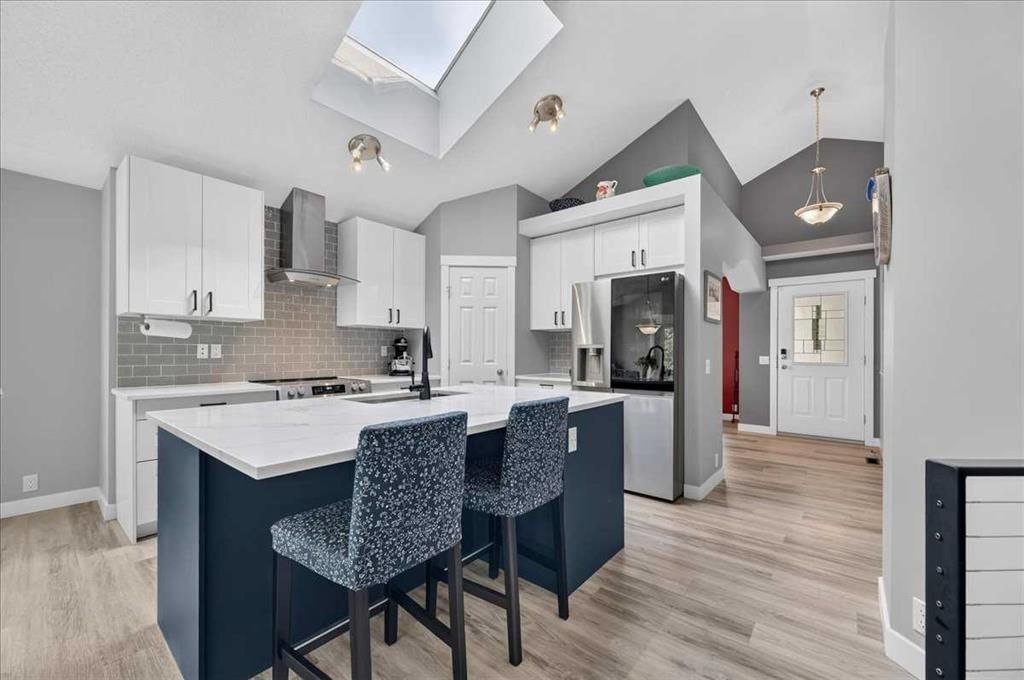 Bright modern kitchen with white cabinets, island seating, stainless steel appliances, and skylight lighting