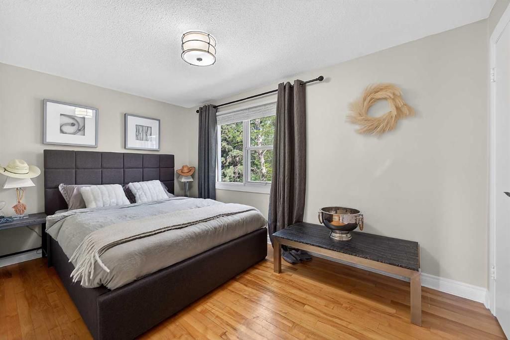 Bright bedroom with a dark bed, gray curtains, wood floor, and a bench by the window.