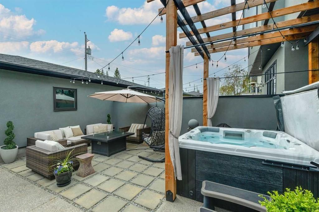 Patio with wicker sofa and chairs beside a hot tub under a wooden pergola