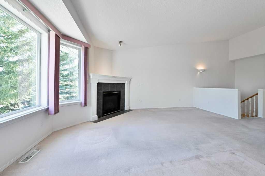 Bright empty living room with large windows, carpeted floor, and a fireplace.