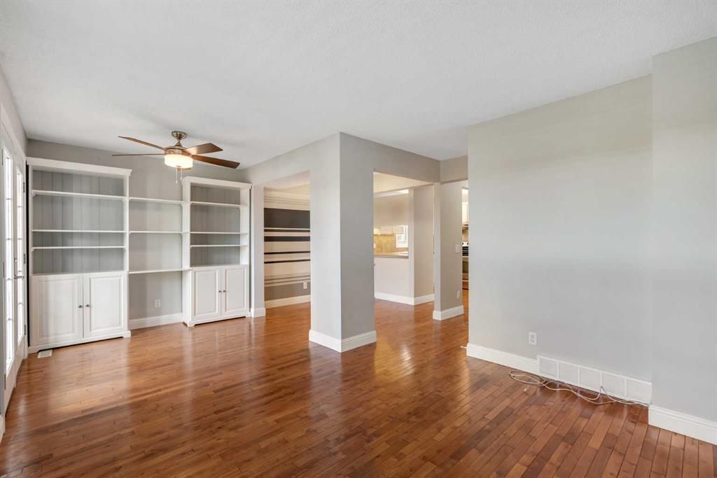 Empty living room with hardwood floors, white built-in cabinets, and a ceiling fan