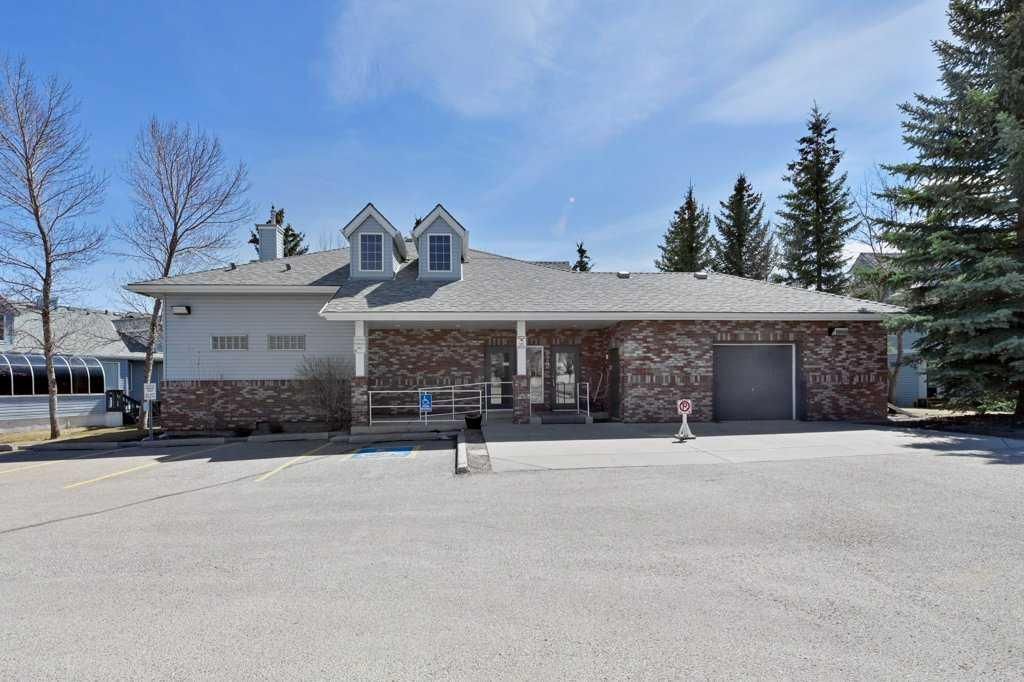 Single-story house with stone exterior, two dormer windows, and a large gravel driveway under a clear blue sky
