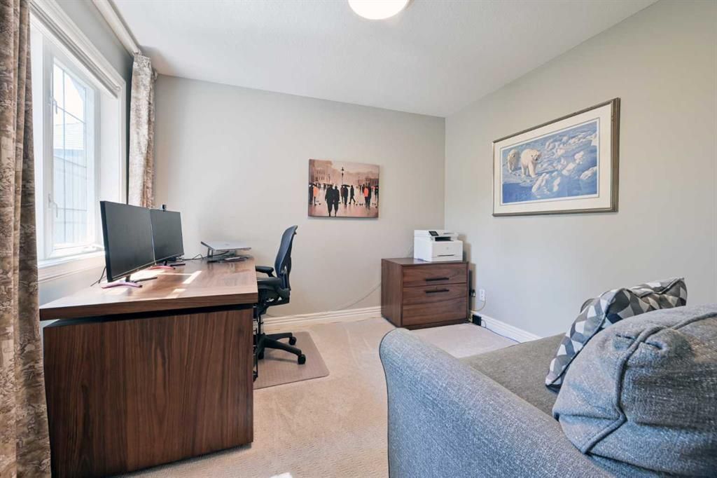 Bright home office with desk, chair, sofa, and dresser in a gray room with wall art and a window.