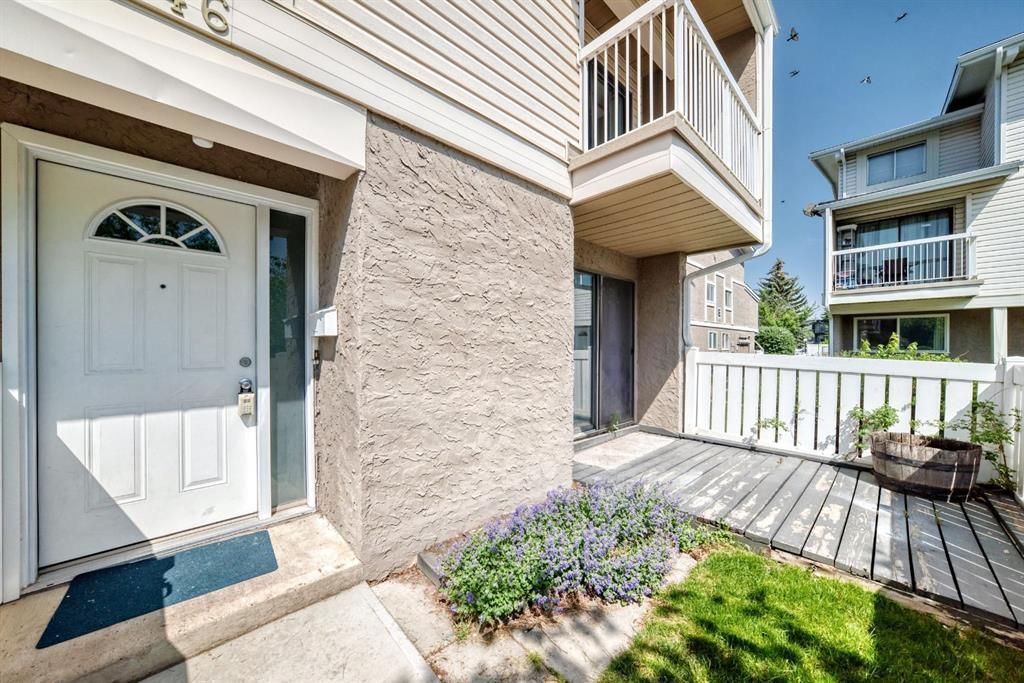 Apartment entrance with white door, wooden deck, and small garden beside a stucco building