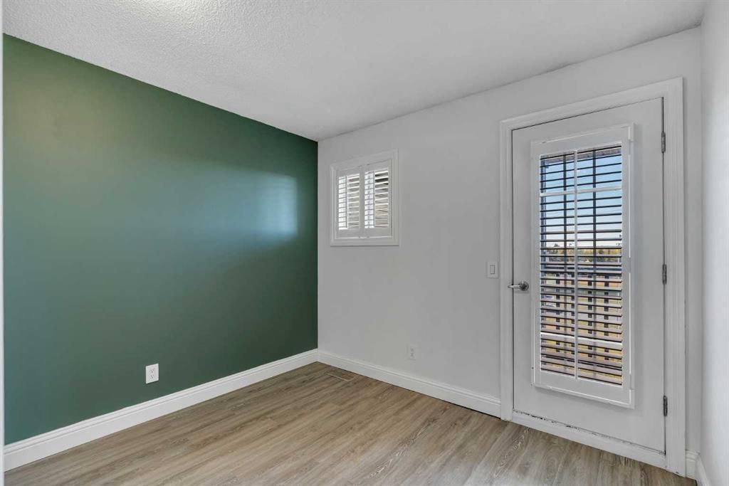 Empty room with green accent wall, white walls, wood flooring, small window, and glass door with blinds